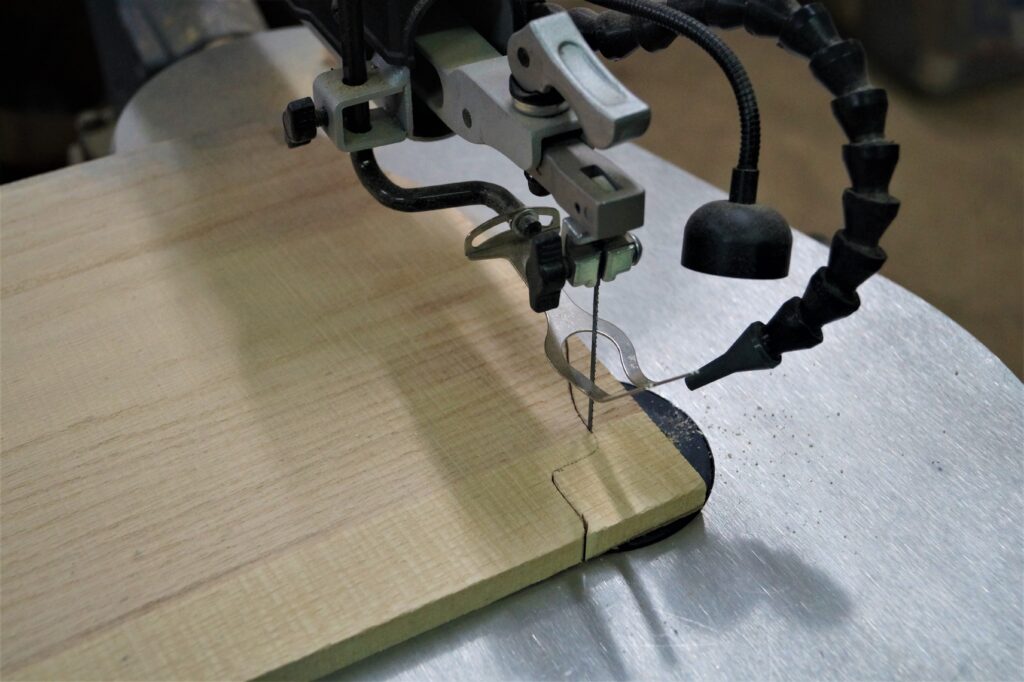 Scroll saw cutting curved design out of piece of wood top of footed wood serving board