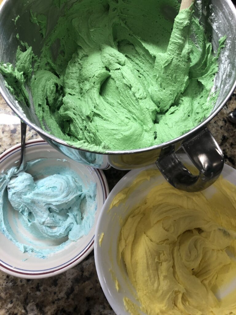 large bowl of green icing, medium bowl of yellow icing, and small bowl of light blue icing