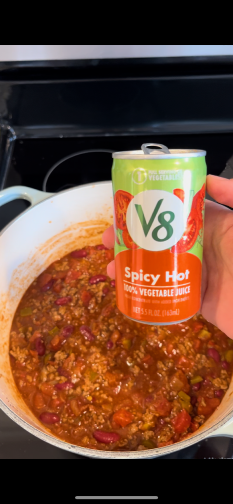 spicy hot V8 held above pot of chili on stovetop