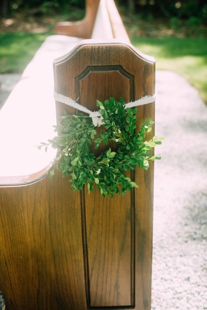 boxwood wreath hanging on end of church pew