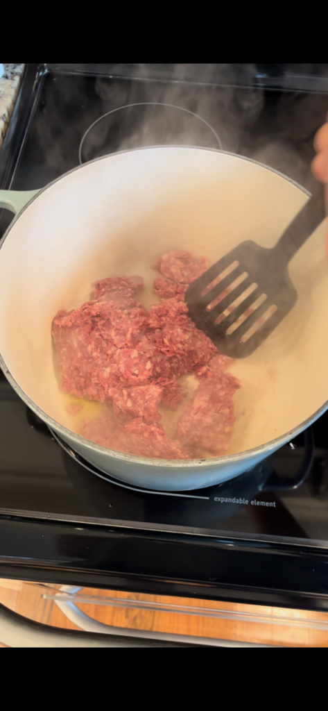 browning ground beef in light blue pot on stovetop with spatula 