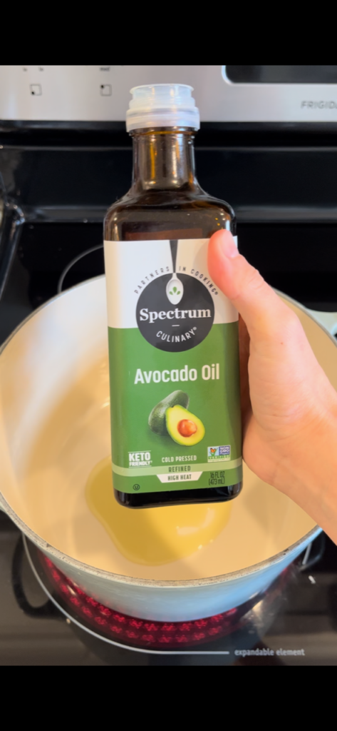 Avocado oil held above blue pot on stovetop