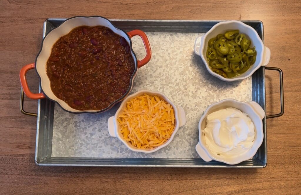 bowls filled with chili, cheddar cheese, jalapenos, and sour cream placed on metal tray